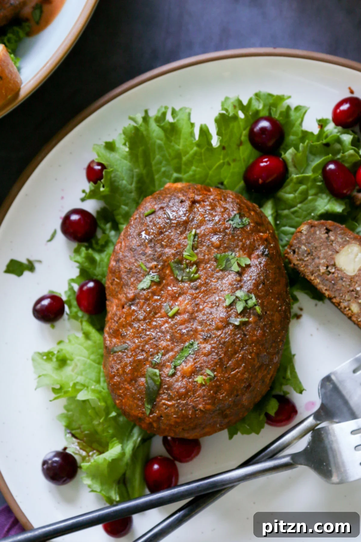 A close-up view of a slice of the savory chickpea loaf on a plate, garnished with fresh lettuce and ruby-red cranberries, highlighting its enticing texture.
