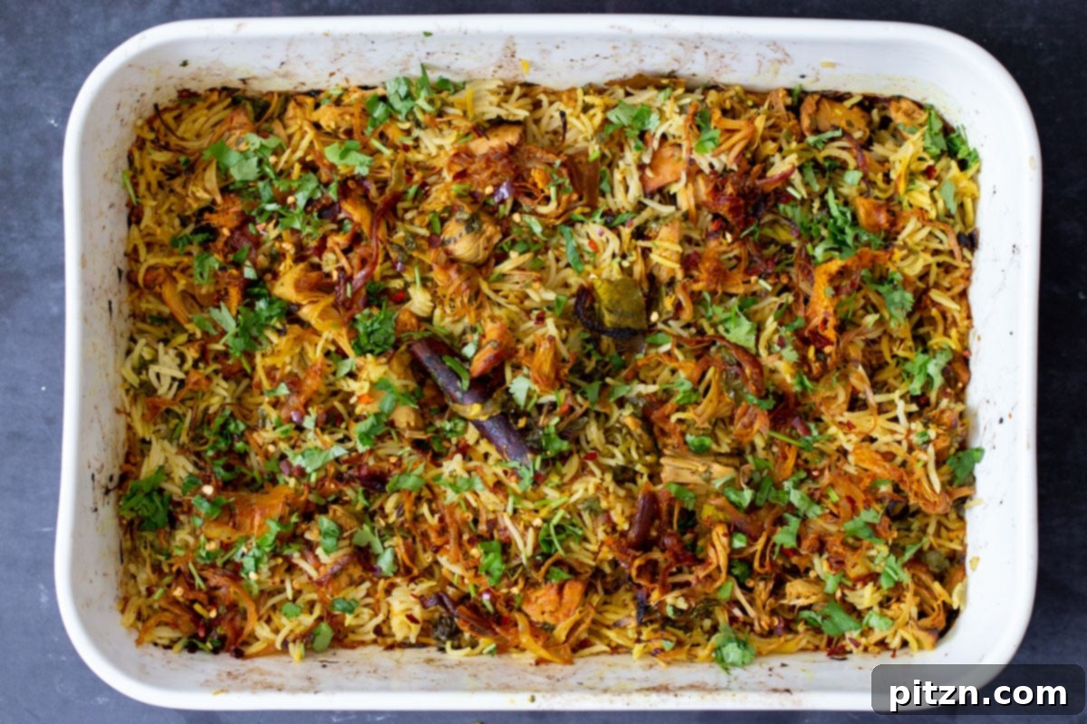 A pan of garnished jackfruit biryani, topped with cashews, herbs, and lemon, ready for serving.