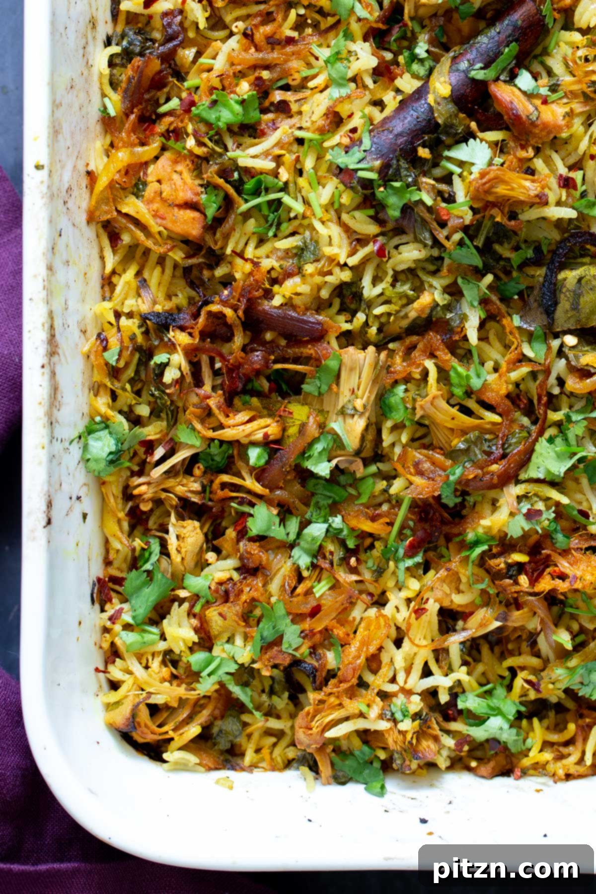 A close-up view of the baked jackfruit biryani still in the pan, showing its golden onions and fluffy rice.