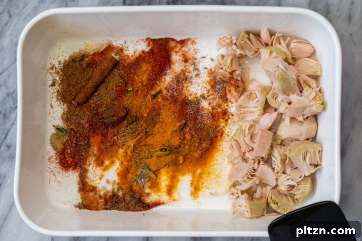 Ground spices being sprinkled over the jackfruit and whole spice mixture in the baking pan.