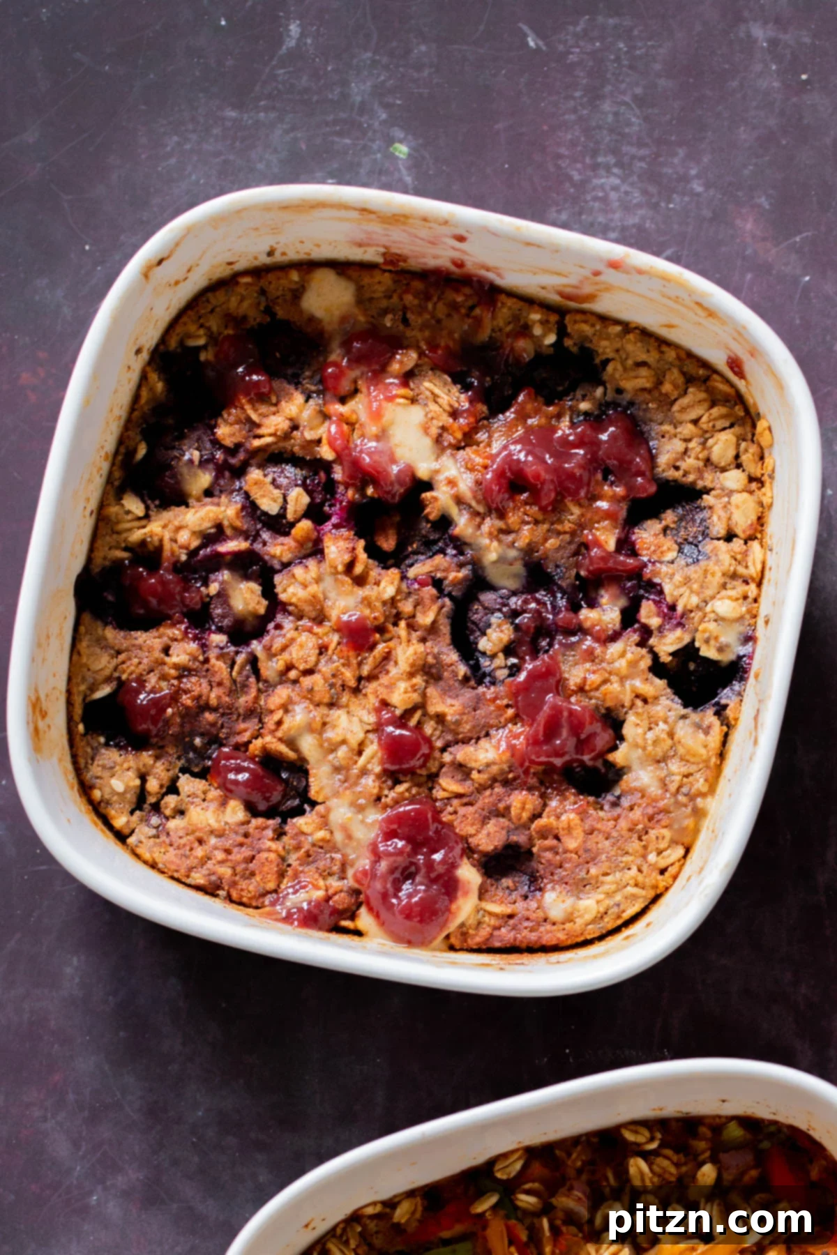 Cozy Baked Oatmeal Gift Mix 3 Close-up photo of baked peanut butter and jelly oatmeal in a small baking dish, topped with fresh blueberries.