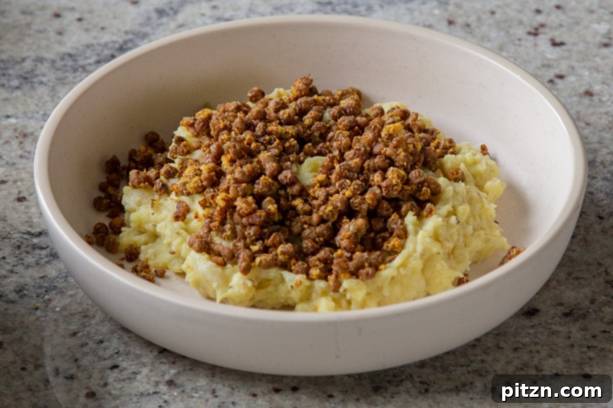 Popped Lentils and Whipped Potatoes 16 Popped lentils being added on top of the creamy potato-cauliflower mash in a serving bowl, showcasing the layering of textures.