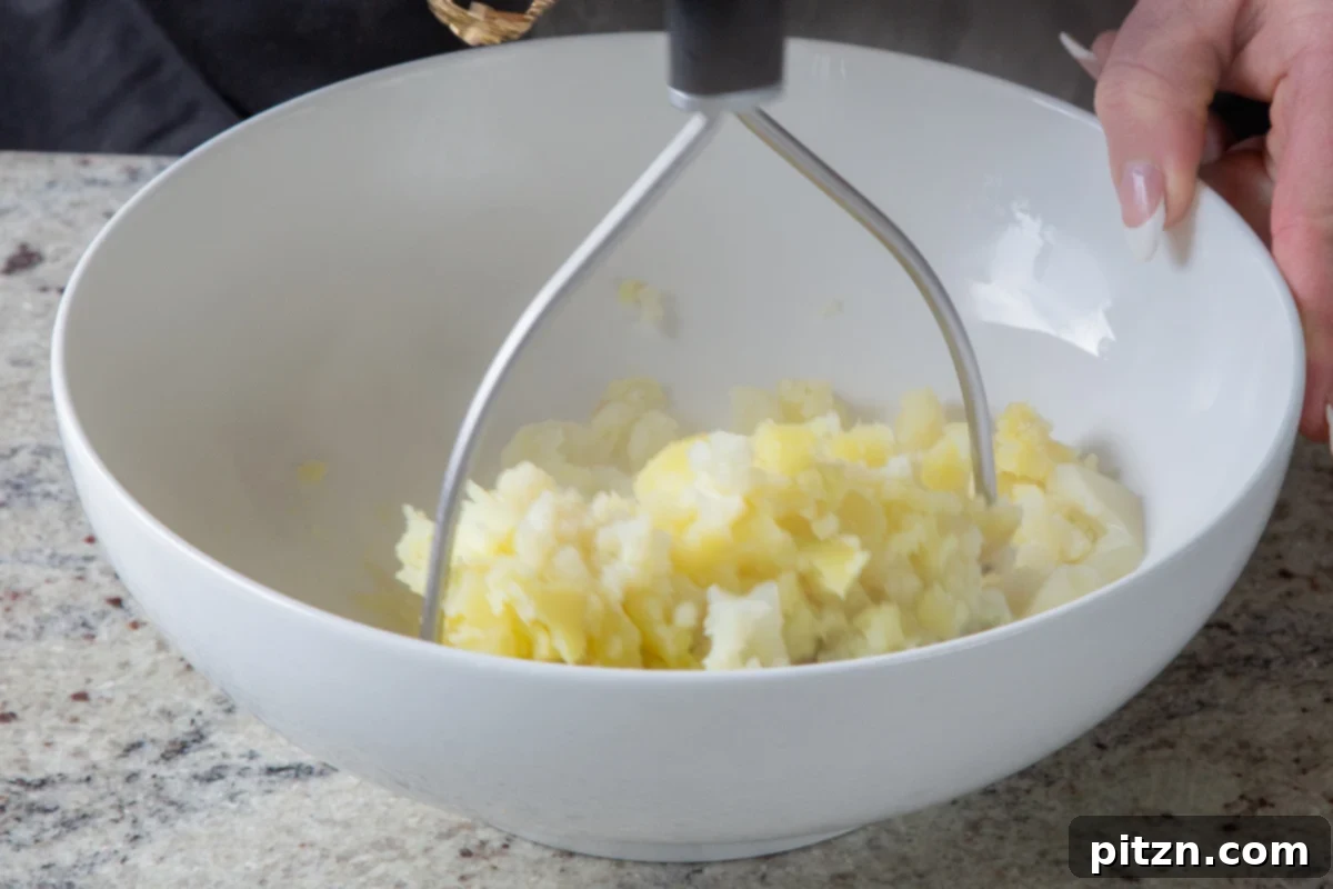 Popped Lentils and Whipped Potatoes 8 A close-up shot of cauliflower and potatoes being mashed in a bowl with a potato masher, achieving a smooth consistency.