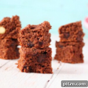 Stack of vegan chocolate brownies on a white wooden surface, with a sprinkle of cocoa powder