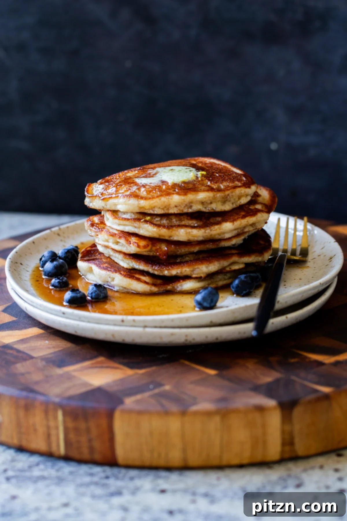 Stack of perfectly golden gluten-free lemon blueberry pancakes, garnished with fresh blueberries and a dusting of powdered sugar, served on a white plate