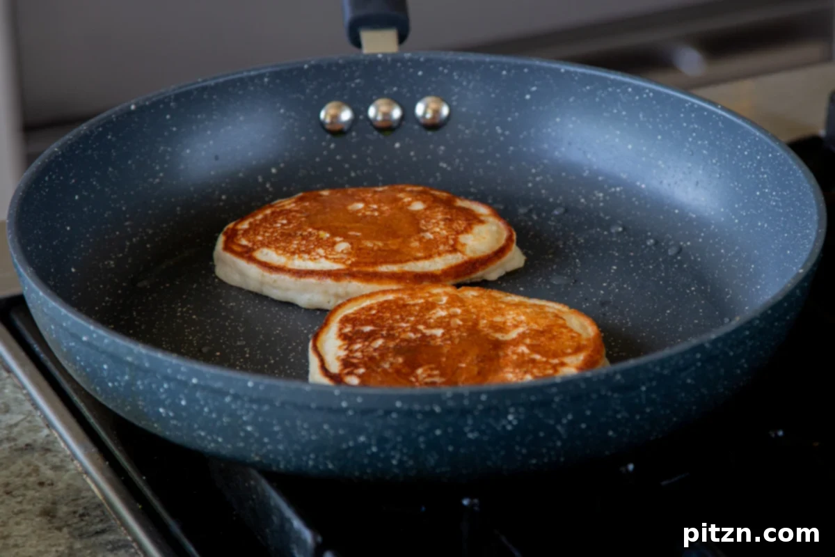 Gluten-free lemon blueberry pancakes cooking on a skillet after being flipped, showing their golden-brown undersides and continued gentle rise as they finish cooking