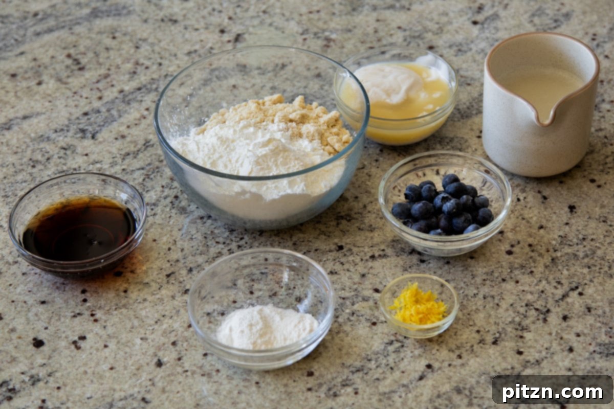 Bowls filled with blanched almond flour, tapioca starch, fresh blueberries, and lemon zest, along with other essential pancake ingredients, arranged neatly on a kitchen counter, ready for mixing.