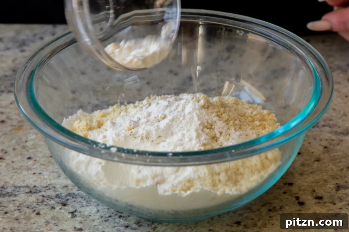 A bowl containing dry ingredients for pancakes, including white almond flour, tapioca starch, and yellow lemon zest, ready to be mixed