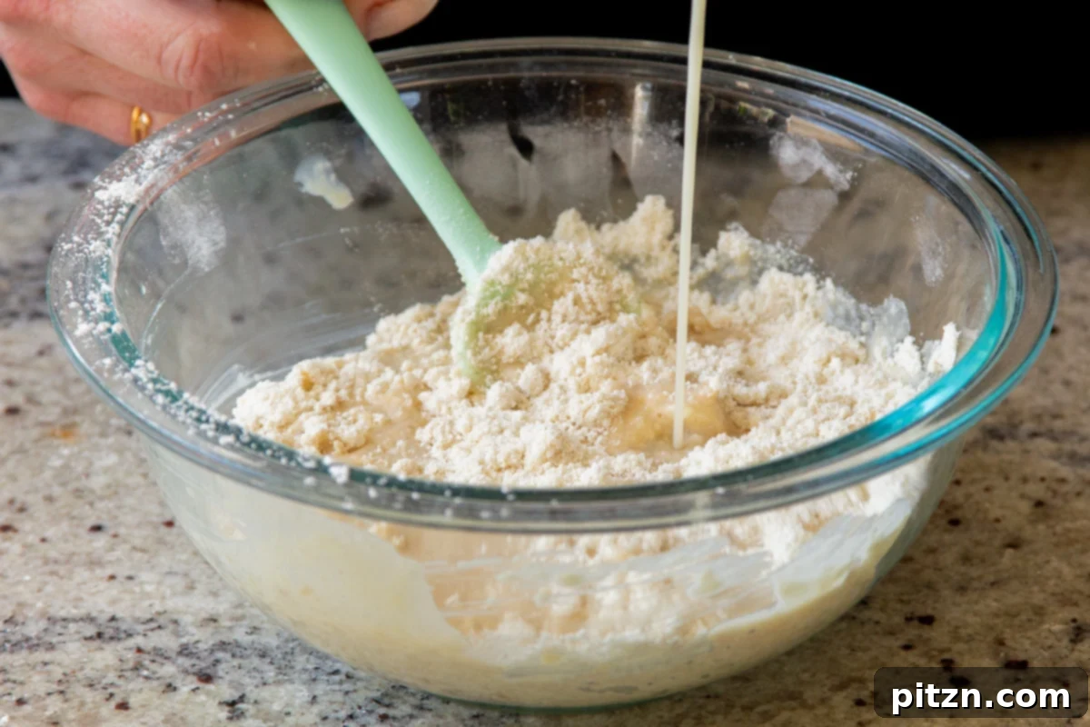 A stream of non-dairy milk being poured into pancake batter in a mixing bowl, illustrating the process of adjusting the batter's consistency