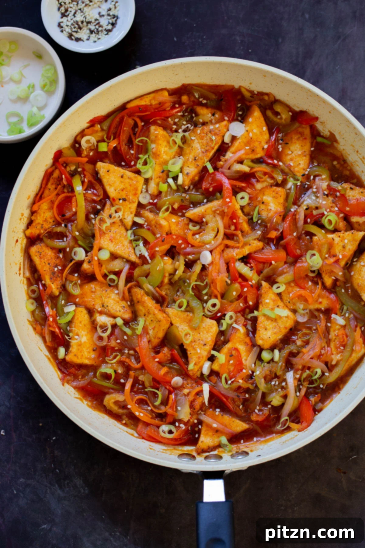 One Pan 30 Minute Schezwan Tofu 2 Crispy Szechuan tofu stir-frying in a pan with green onions and sesame seeds, ready to serve.
