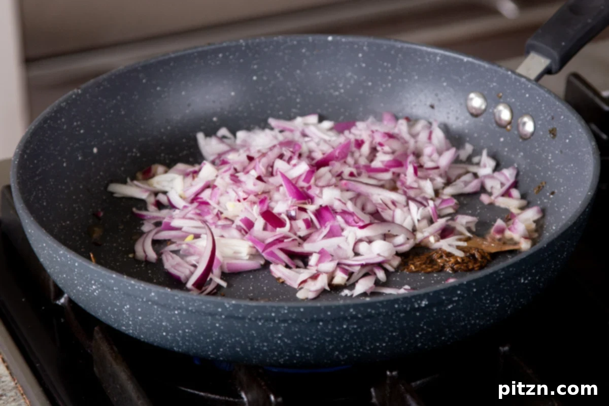 One Pot White Bean Do Pyaza Curry 9 Finely chopped red onions being added to the pan with toasted whole spices, ready to caramelize.