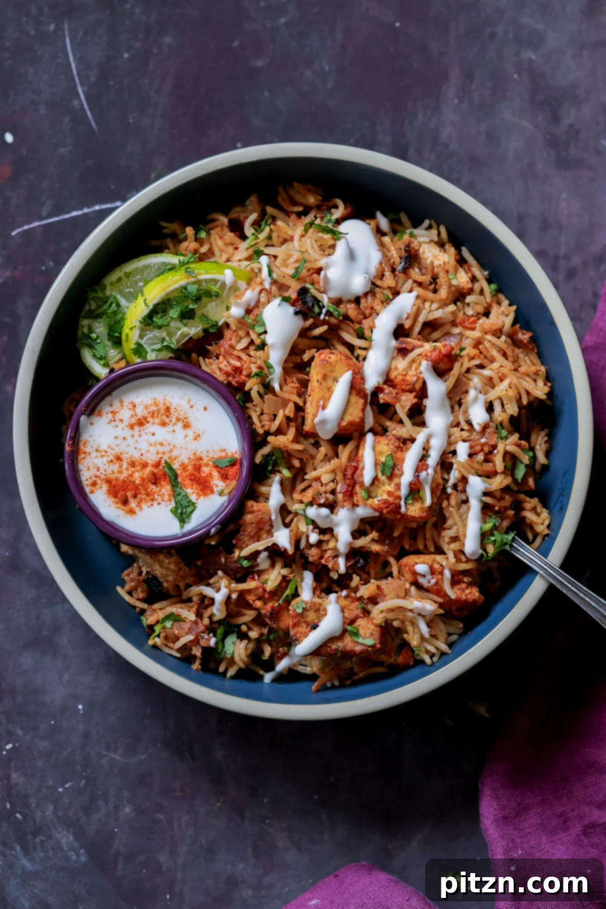A vibrant bowl of Lucknowi Biryani, generously topped with fresh raita, with an extra ramekin of raita on the side, ready to be served.