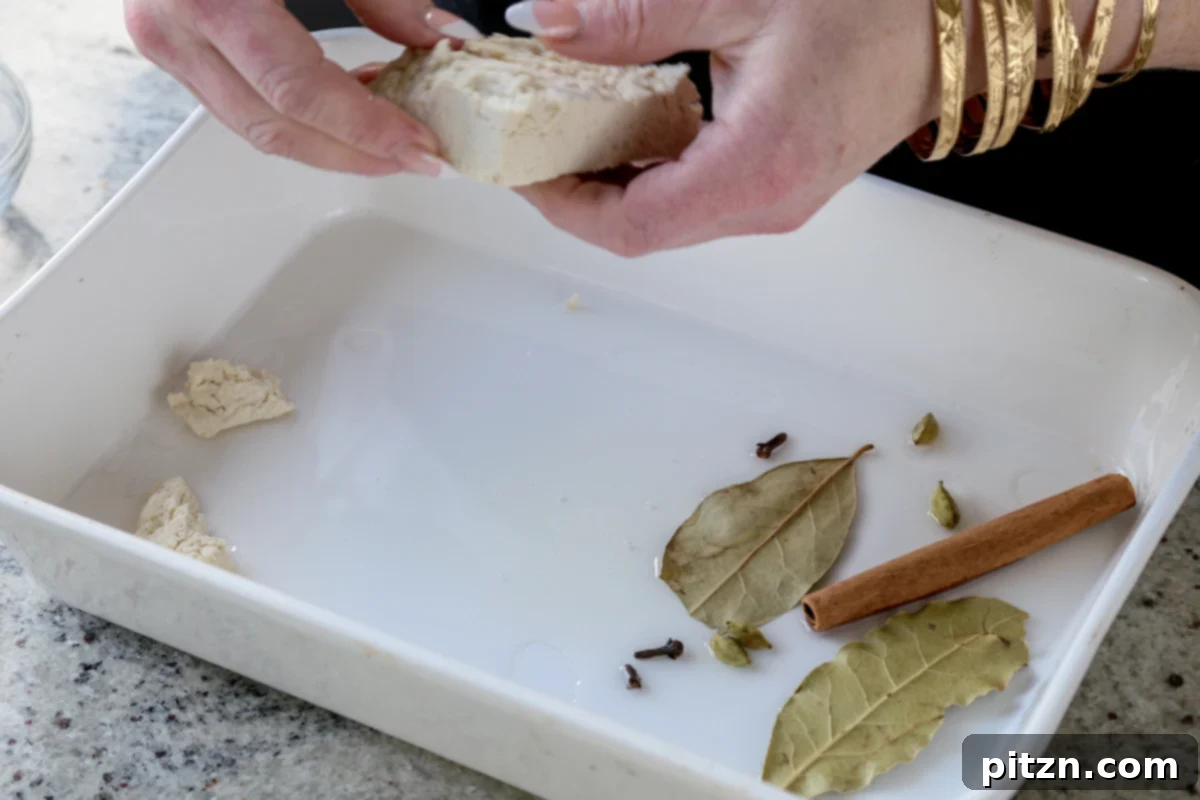 Hands are shown tearing firm tofu into rustic 1-inch pieces directly into one side of a baking pan, preparing it for baking.