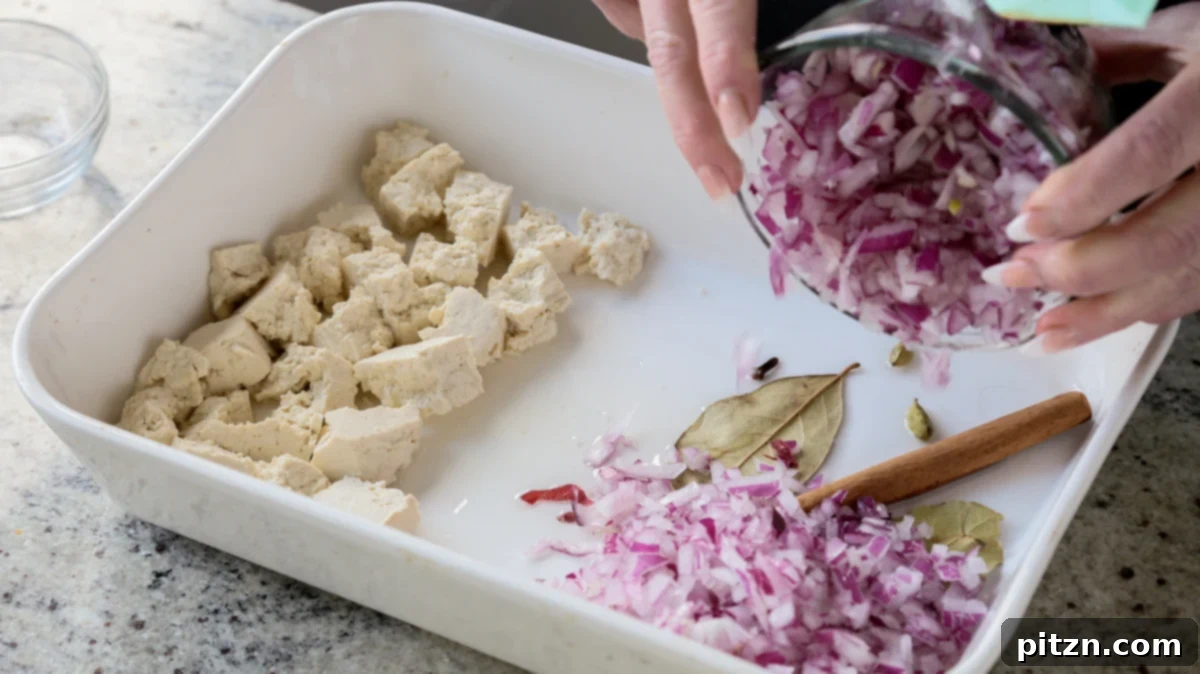 Chopped red onions are added to the other side of the baking pan, opposite the torn tofu, creating distinct sections for initial baking.