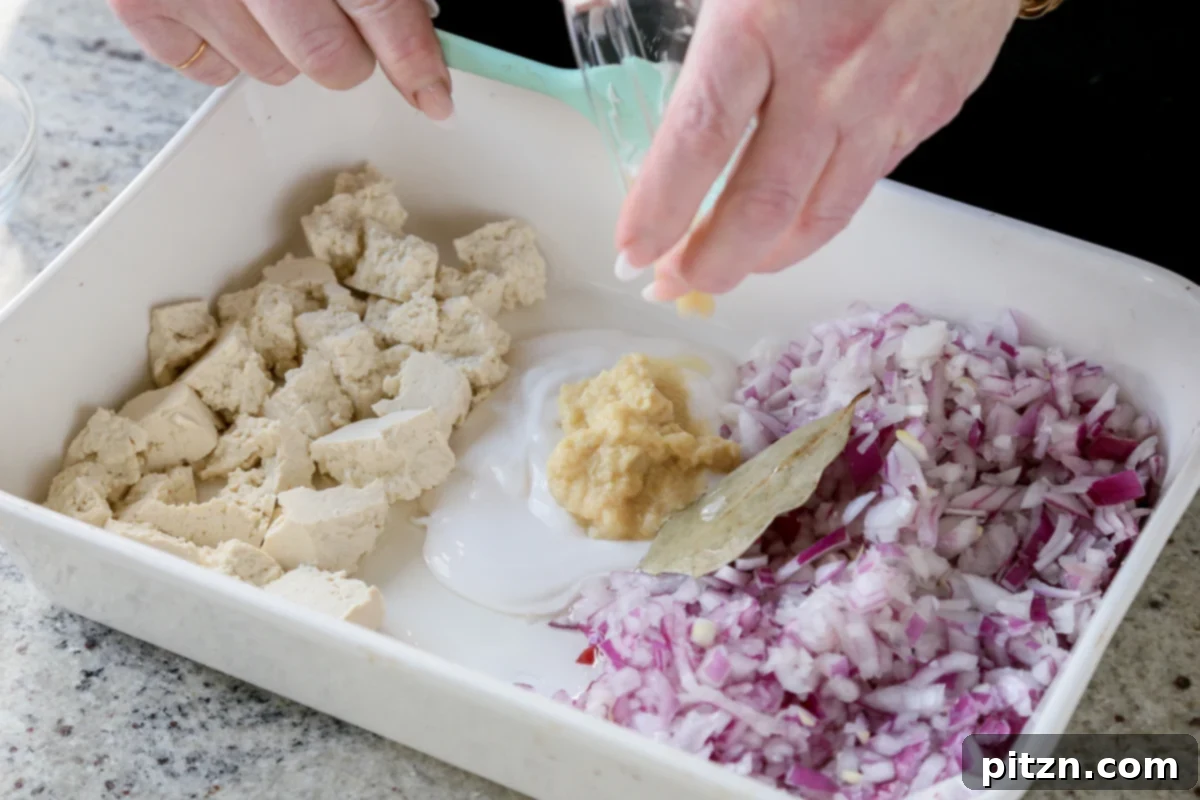 A dollop of ginger garlic paste and a spoonful of non-dairy yogurt are placed in the center of the baking pan, ready to be mixed with spices.