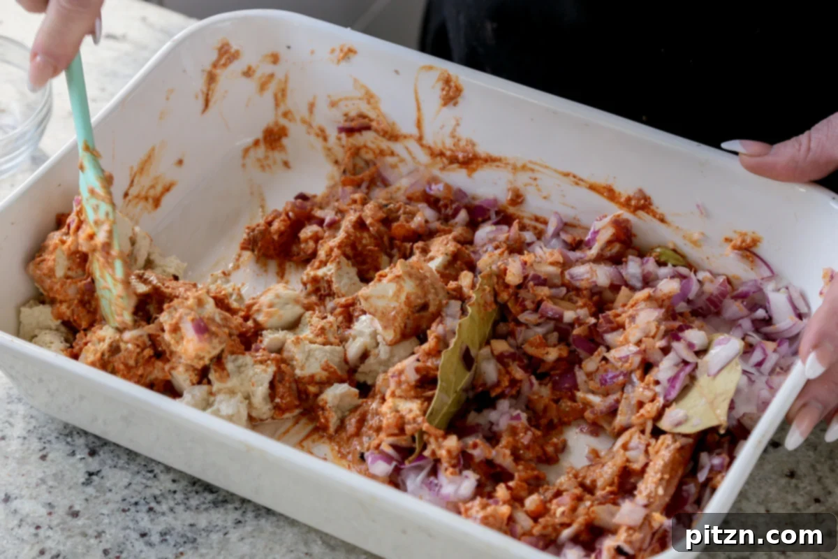 Tofu and chopped onions, distinctly separated, are shown being mixed with the flavorful spice paste in a baking pan.