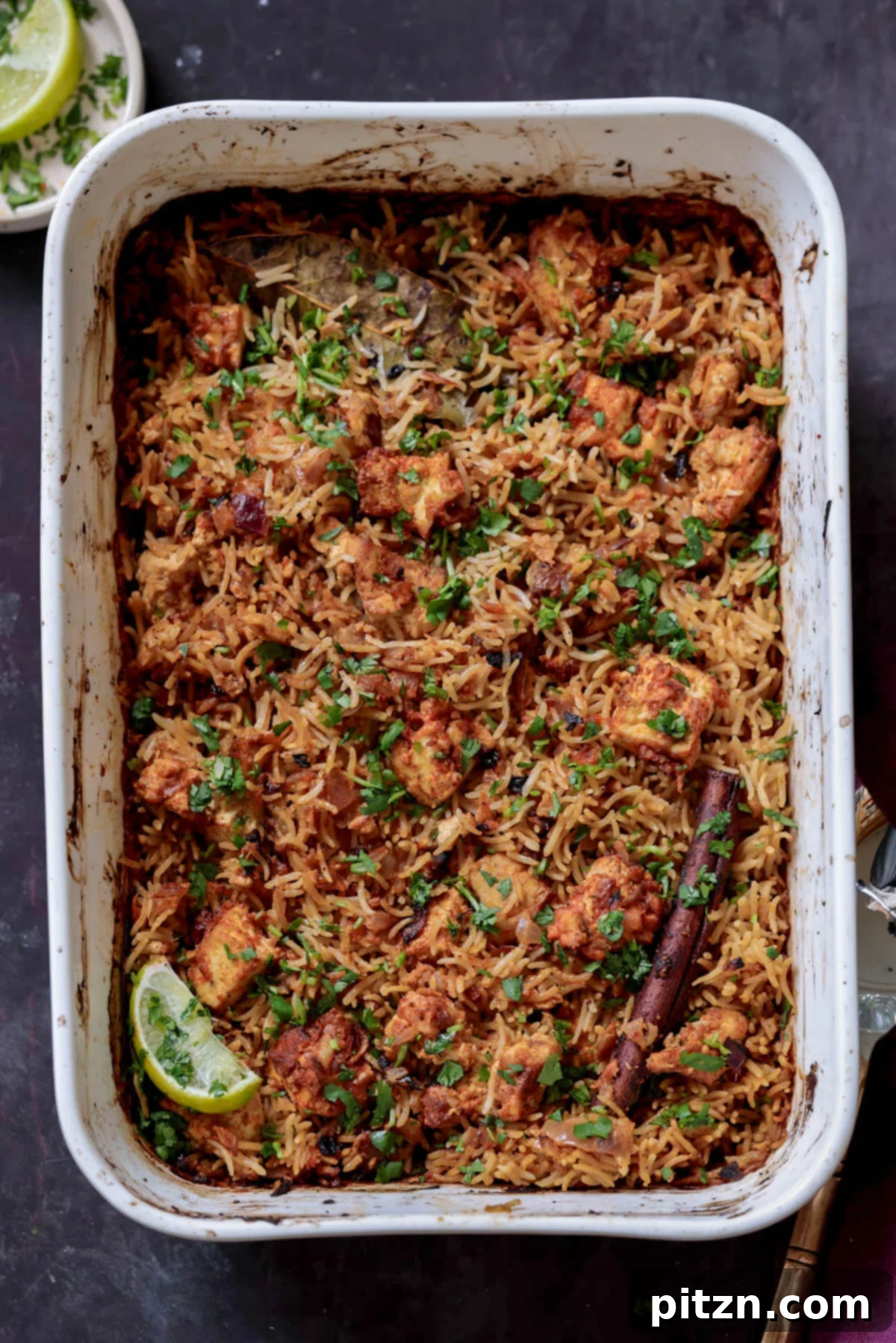 Close-up of freshly baked Lucknowi Biryani steaming hot in a rectangular baking pan, showcasing its aromatic layers.