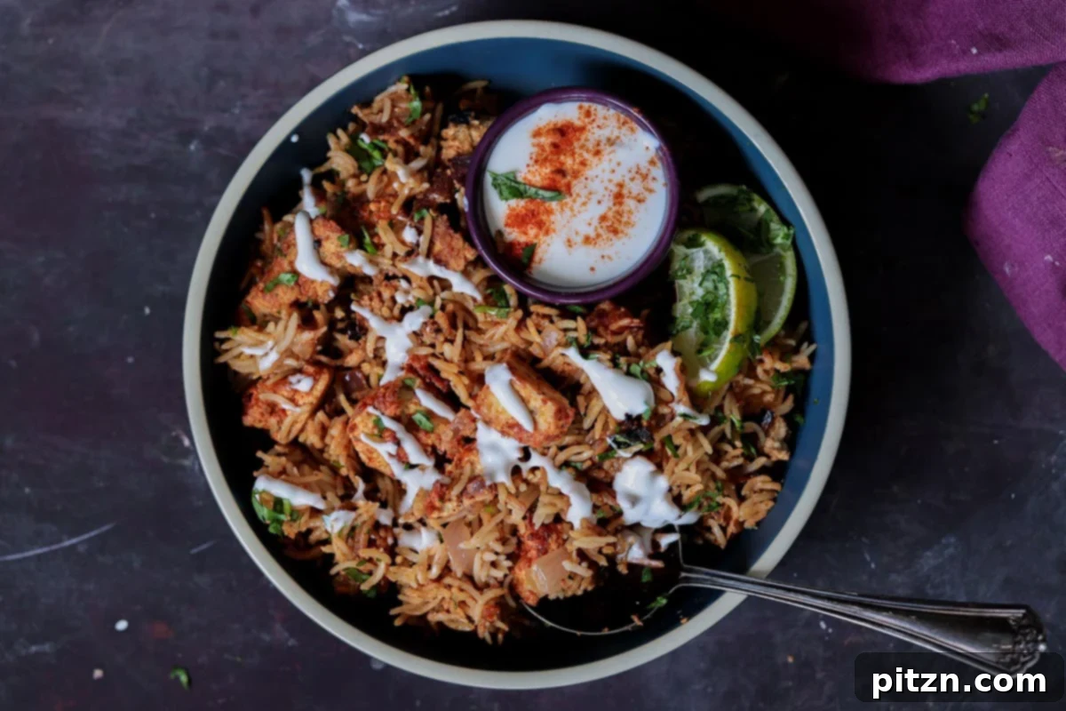 A beautifully presented bowl of Lucknowi Biryani, garnished with fresh raita and cilantro, accompanied by a small ramekin of raita on the side for individual serving.