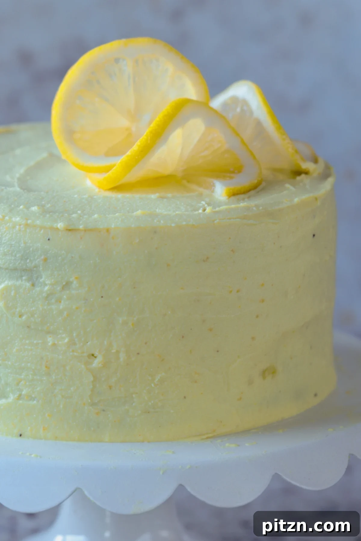 Zesty Vegan Lemon Cloud Cake 2 Close-up of a frosted vegan lemon cake topped with fresh lemon slices, ready for serving