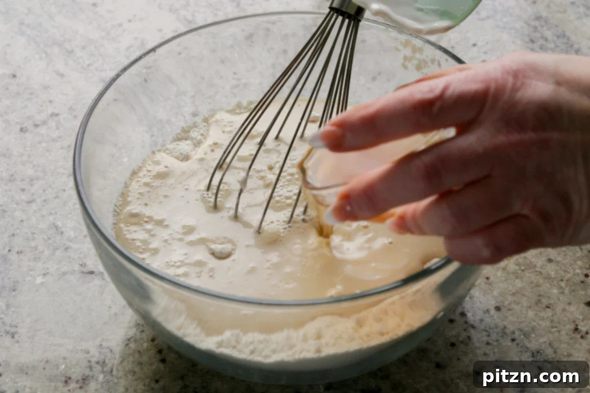 Zesty Vegan Lemon Cloud Cake 12 Wet ingredients being poured into the bowl of dry ingredients for the vegan lemon cake