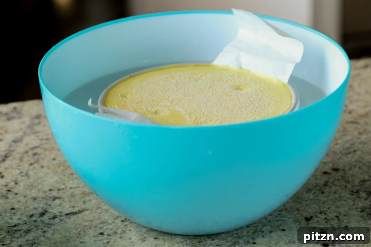 Zesty Vegan Lemon Cloud Cake 24 The chilled vegan lemon cake in its pan being placed into a bowl of hot water to aid in release