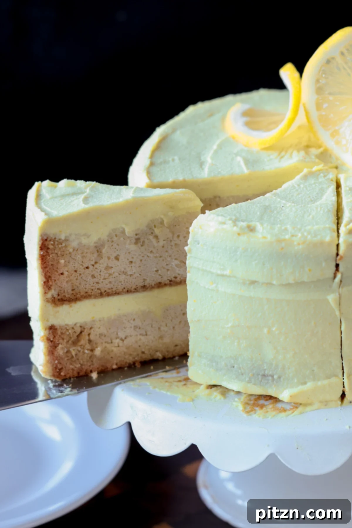 Zesty Vegan Lemon Cloud Cake 4 A slice of vegan lemon cake being carefully removed from a cake stand, highlighting the creamy layers