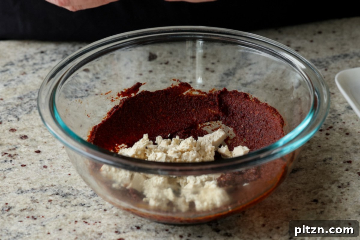 Adding crumbled tofu into the bowl containing the prepared seasoning paste, ready to be mixed for the chorizo tofu.