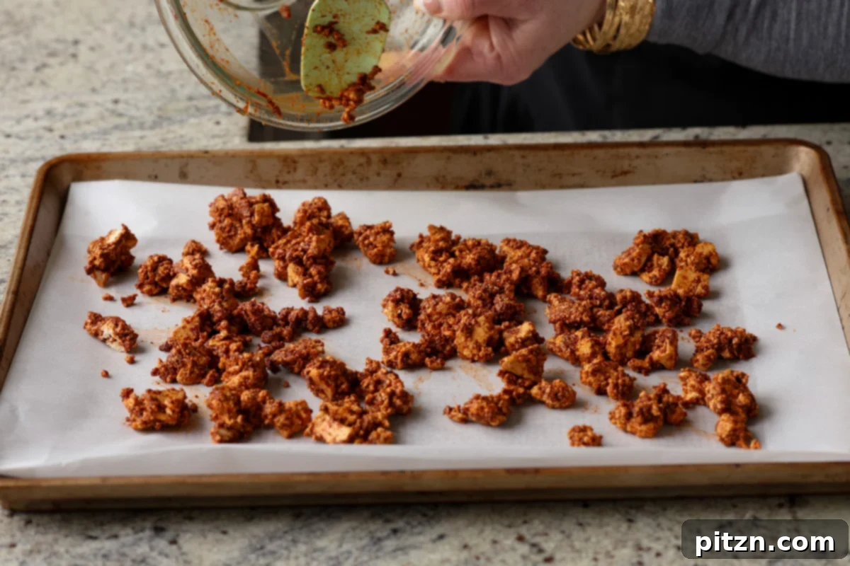 Marinated chorizo tofu spread evenly onto a parchment-lined baking sheet, prepared for baking to a crispy finish.