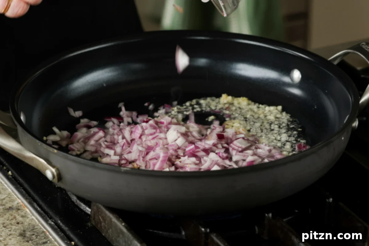 Minced garlic and chopped onions sautéing in a frying pan, creating an aromatic base for the bean mixture.