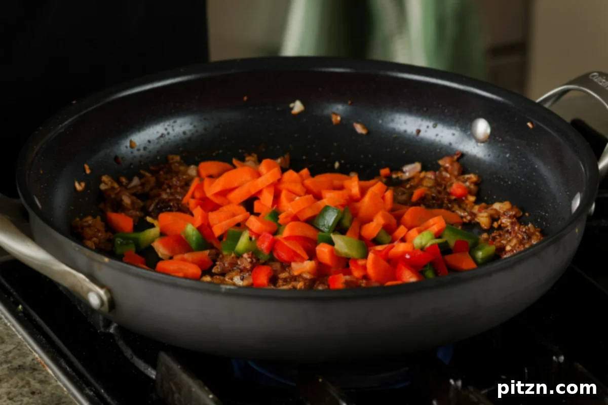 Adding chopped carrots and bell peppers to the sautéed garlic and onions in the pan, for the black bean and lentil stew.