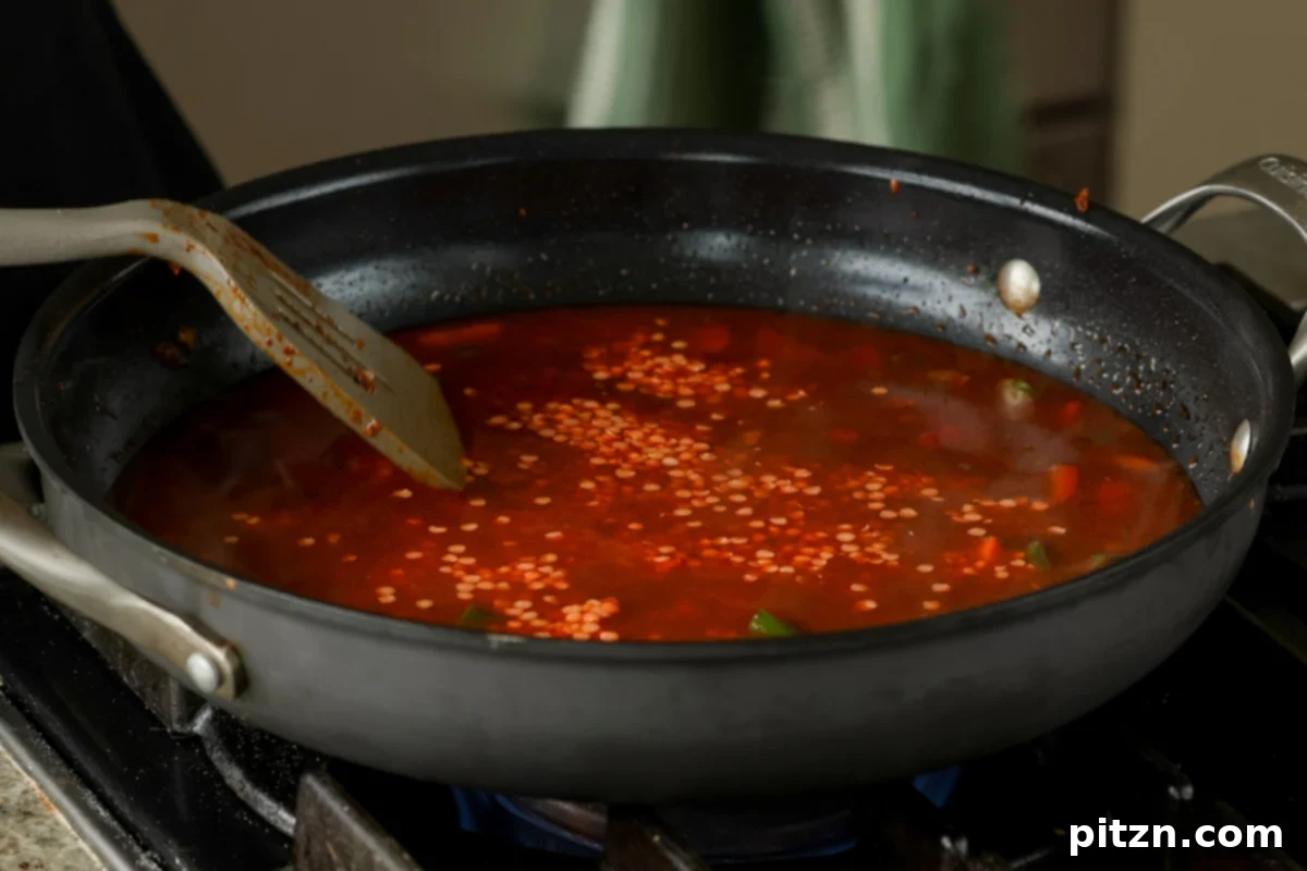 Adding dried red lentils to the simmering vegetables and spices in the pan, to create a thick, hearty stew.