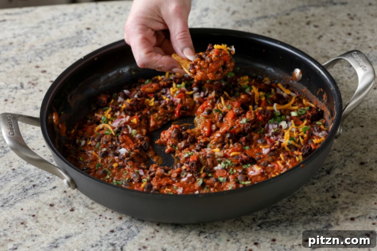 A tortilla chip being dipped into the finished pan of black beans and lentils, showcasing its thick and appetizing texture.