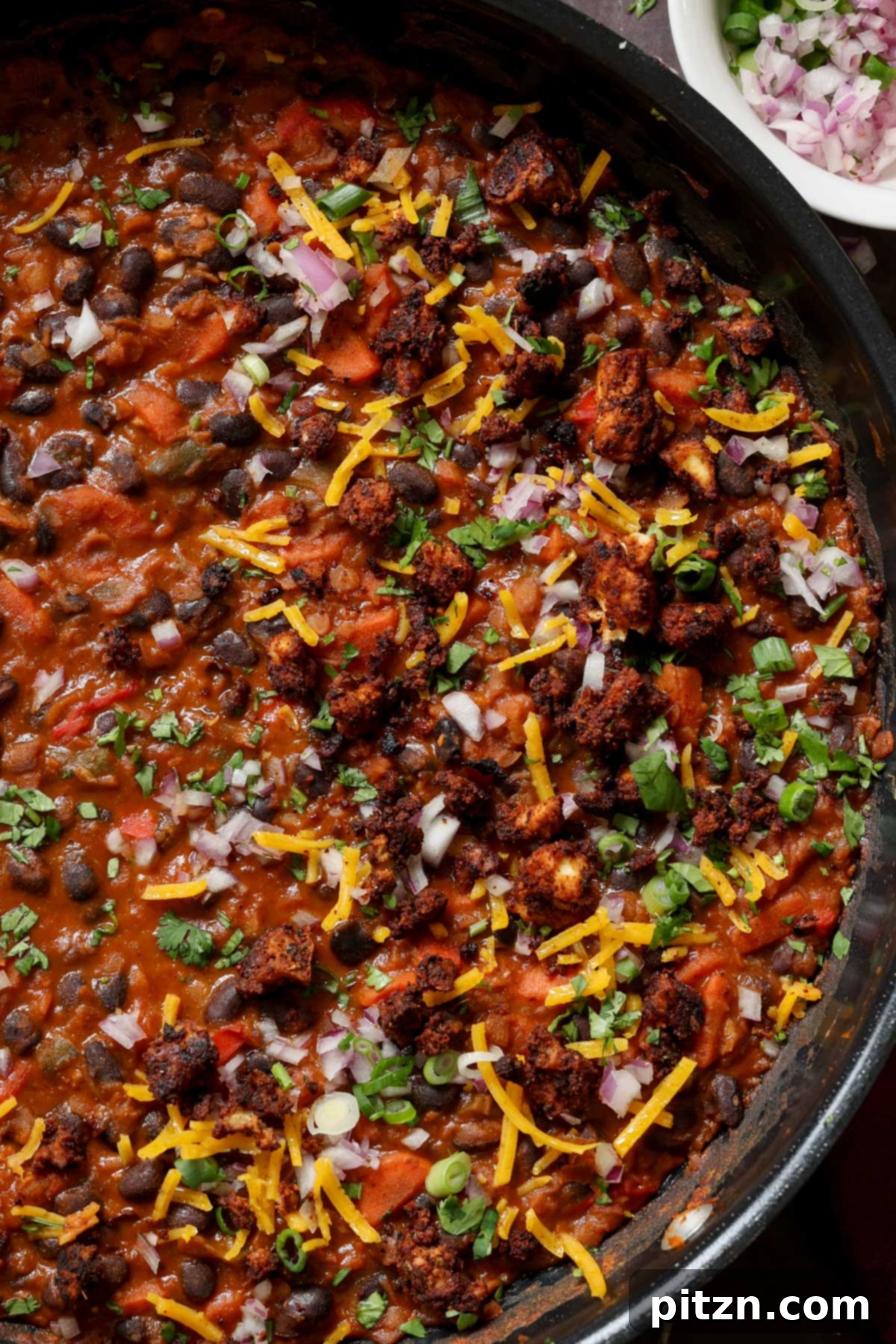 A detailed close-up of the cooked black beans and red lentils in a pan, showcasing the texture of the beans and the savory sauce, garnished lightly.