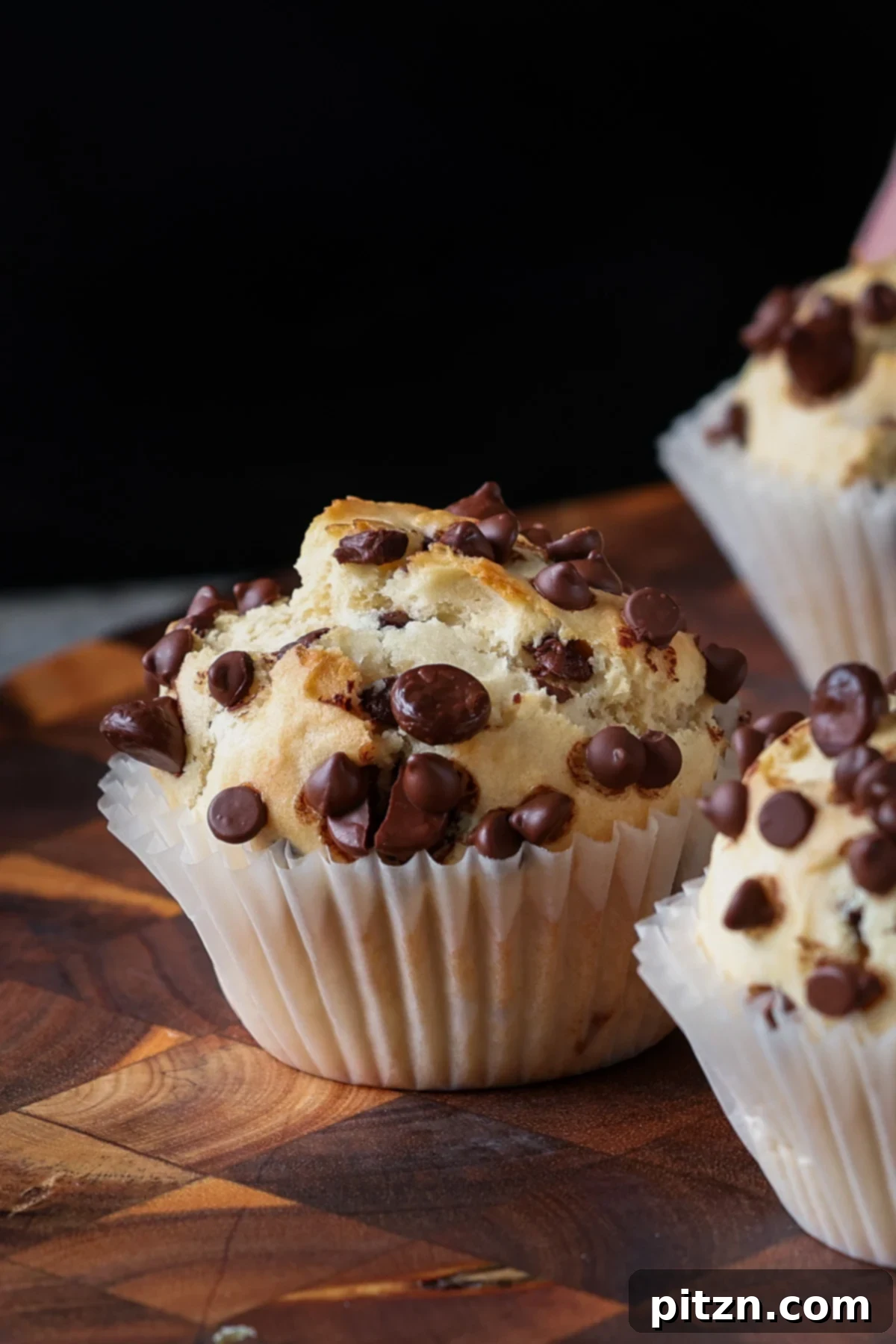 Unbelievably Fluffy Vegan Gluten-Free Chocolate Chip Muffins 2 A freshly baked vegan chocolate chip muffin on a rustic wooden cutting board, showcasing its golden brown top and visible chocolate chips.