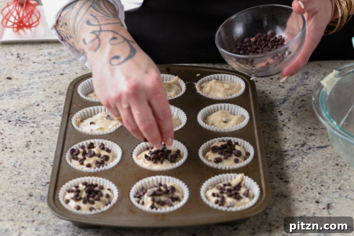Unbelievably Fluffy Vegan Gluten-Free Chocolate Chip Muffins 14 A hand sprinkling extra chocolate chips on top of each muffin in the pan before baking.