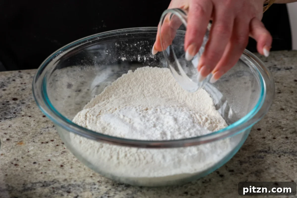 Unbelievably Fluffy Vegan Gluten-Free Chocolate Chip Muffins 8 A hand adding dry ingredients like flour, baking powder, and salt into a mixing bowl.