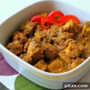A spinach tomato curry in a white bowl with red pepper garnish