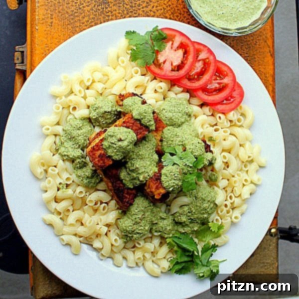 A wider shot of the pasta dish, highlighting the generous portion size and vibrant green pesto with red tomato slices.