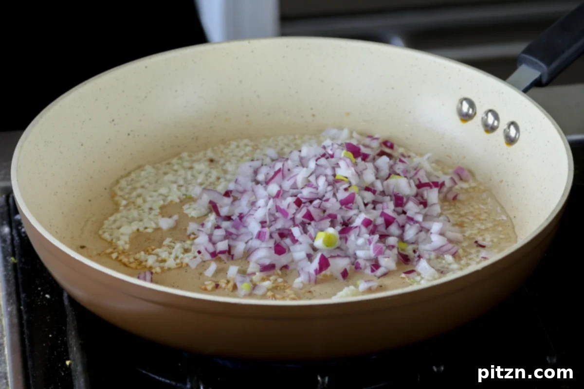 Chopped white onion being carefully added to the hot skillet, joining the fragrant garlic and olive oil mixture.