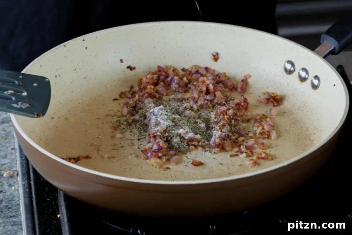 A mix of aromatic dry spices, including onion powder and black pepper, being sprinkled into the skillet with the sautéed aromatics.
