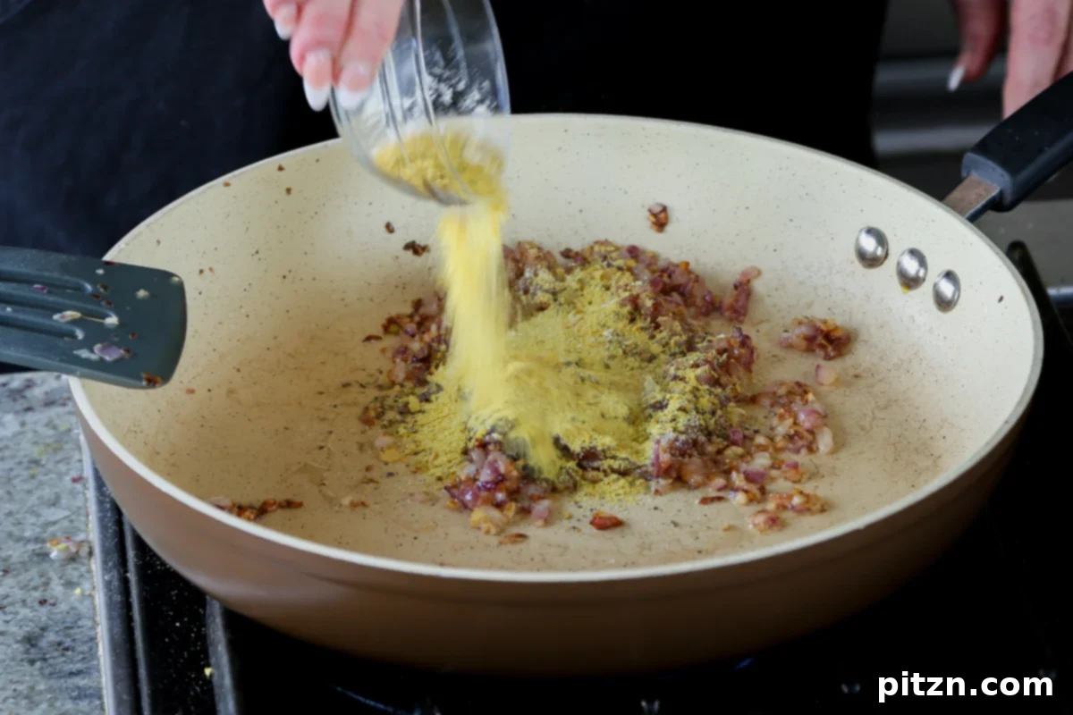 Nutritional yeast being generously added to the pan, contributing its signature cheesy, umami depth to the sauce.