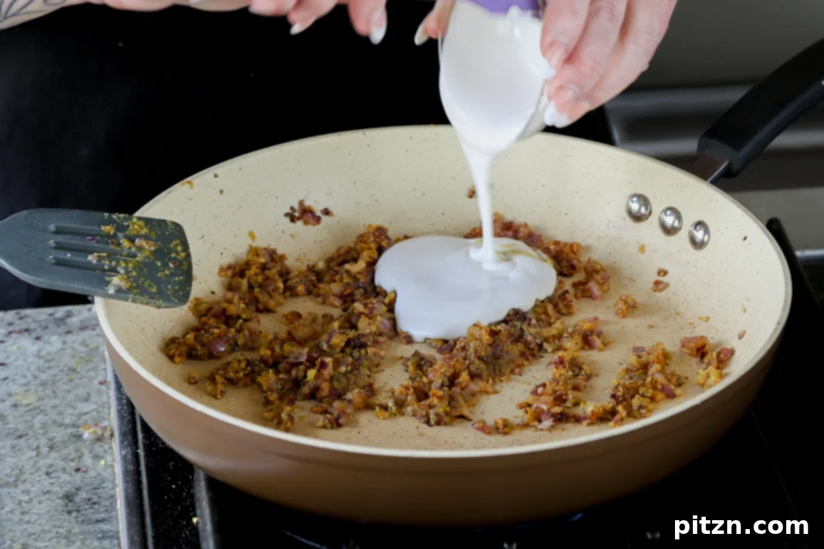 Smooth, unsweetened non-dairy yogurt being stirred into the fragrant mixture in the skillet, forming a creamy and rich sauce base.