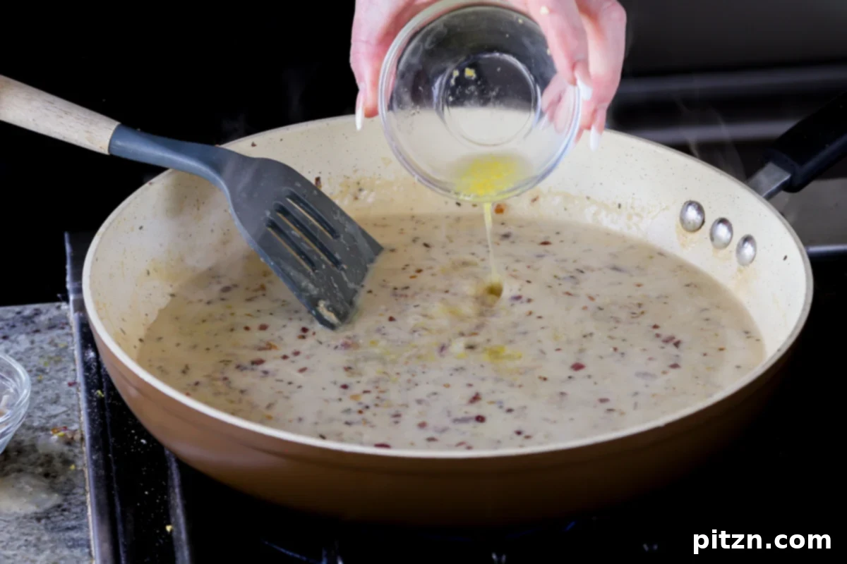 Freshly squeezed lemon juice being poured into the simmering creamy sauce in the pan, adding essential brightness and tang.