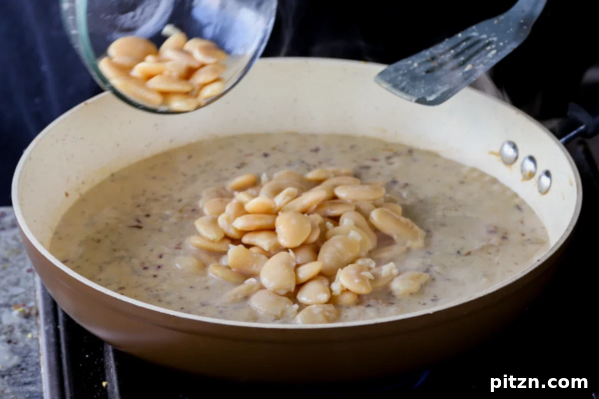 Drained, plump butter beans being gently folded into the luscious garlic lemon sauce in the pan, ensuring even coating.