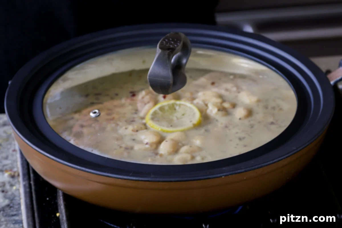 The pan of butter beans simmering gently under a lid, allowing the rich garlic lemon flavors to deeply infuse into the beans.