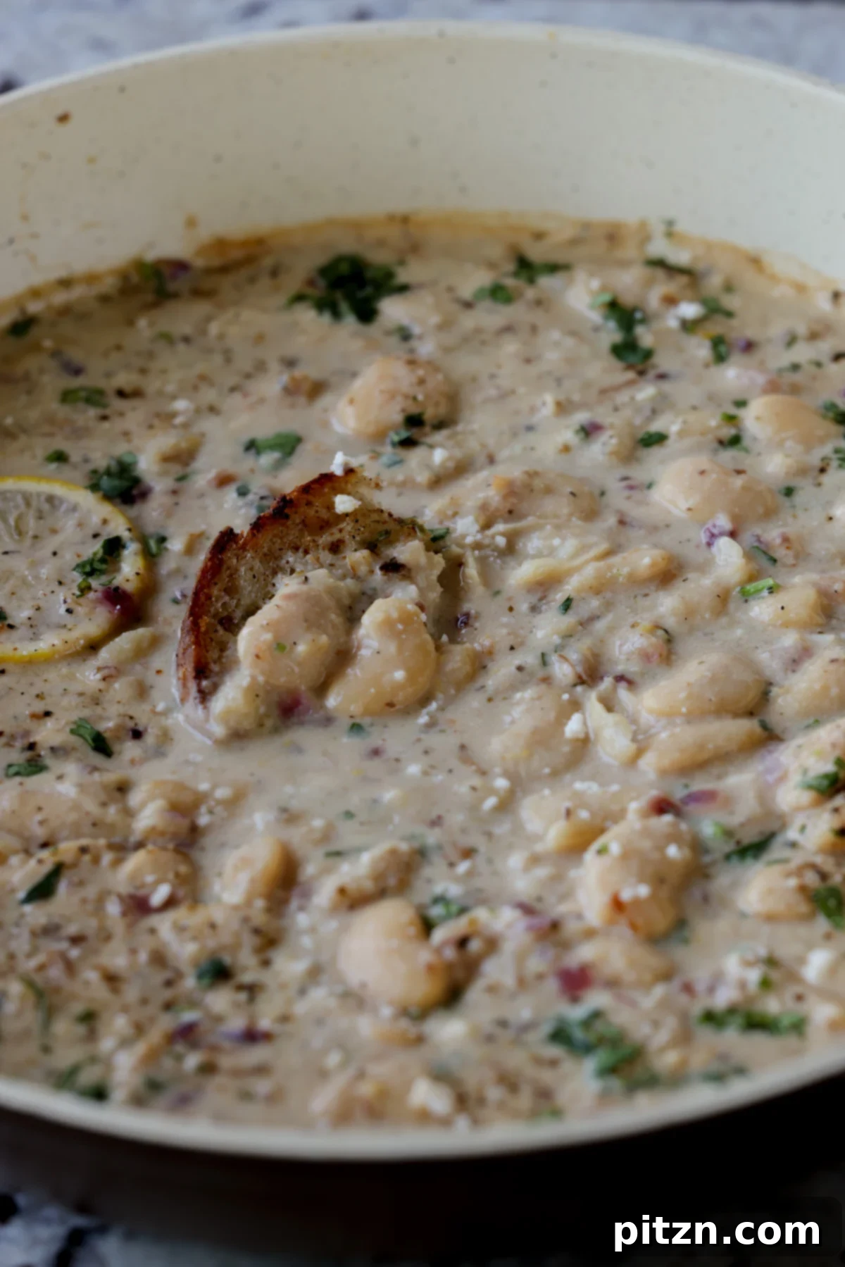 A pan of utterly delicious lemon garlic butter beans, beautifully garnished with fresh parsley and black pepper, with a piece of perfectly toasted sourdough bread on the side, ready for a comforting meal.