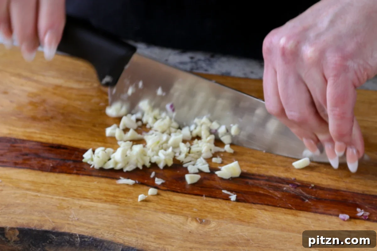 Close-up of freshly minced garlic cloves on a cutting board, prepared for sautéing and adding robust flavor to the dish.