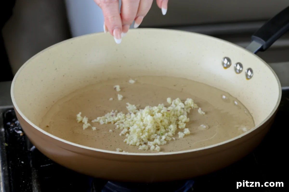 Minced garlic sizzling gently in golden olive oil in a hot skillet, releasing its pungent aroma as it cooks.