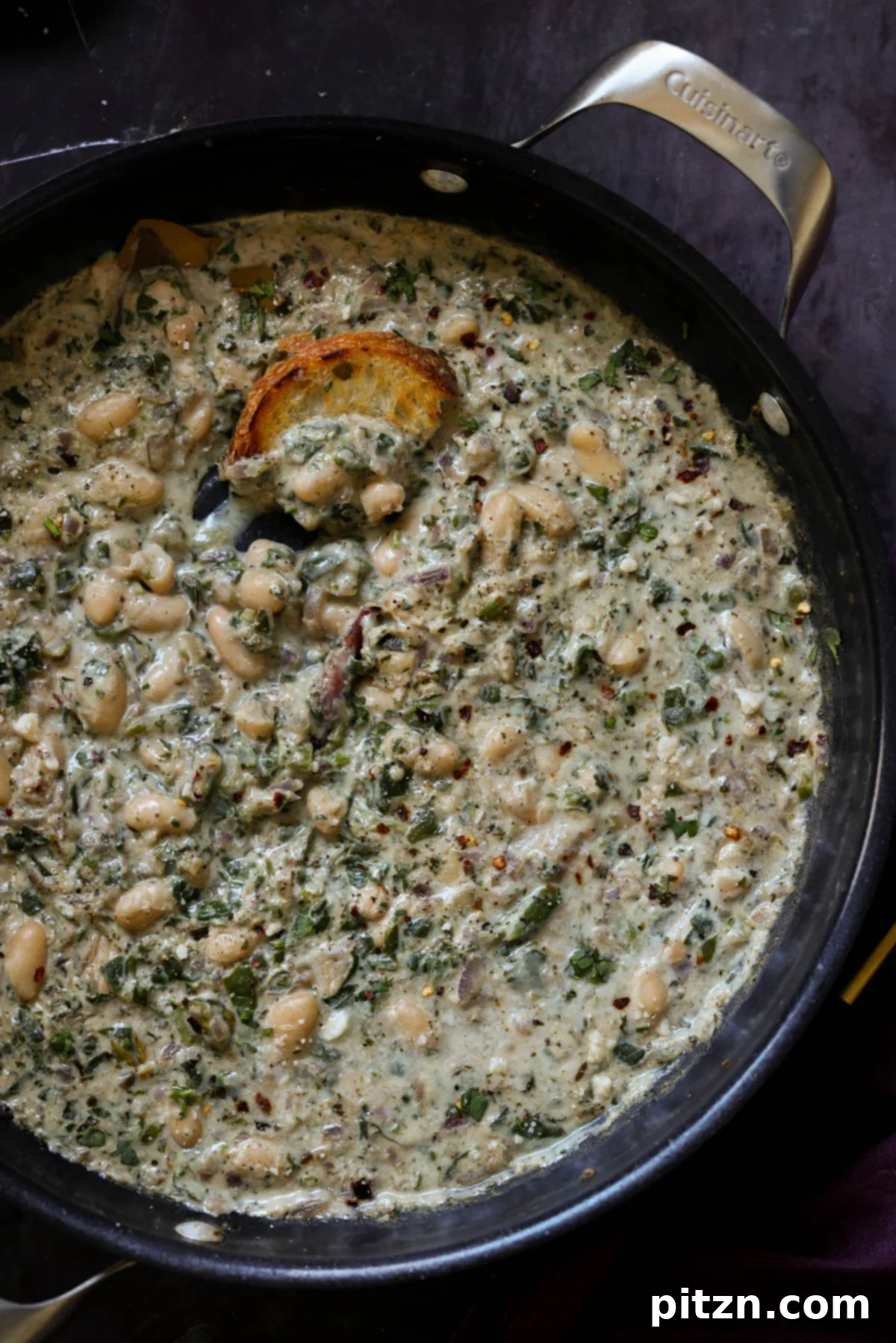 A close-up of Kali Mirch Beans simmering in a pan, accompanied by a piece of toasted sourdough bread, highlighting the creamy texture and aromatic spices.