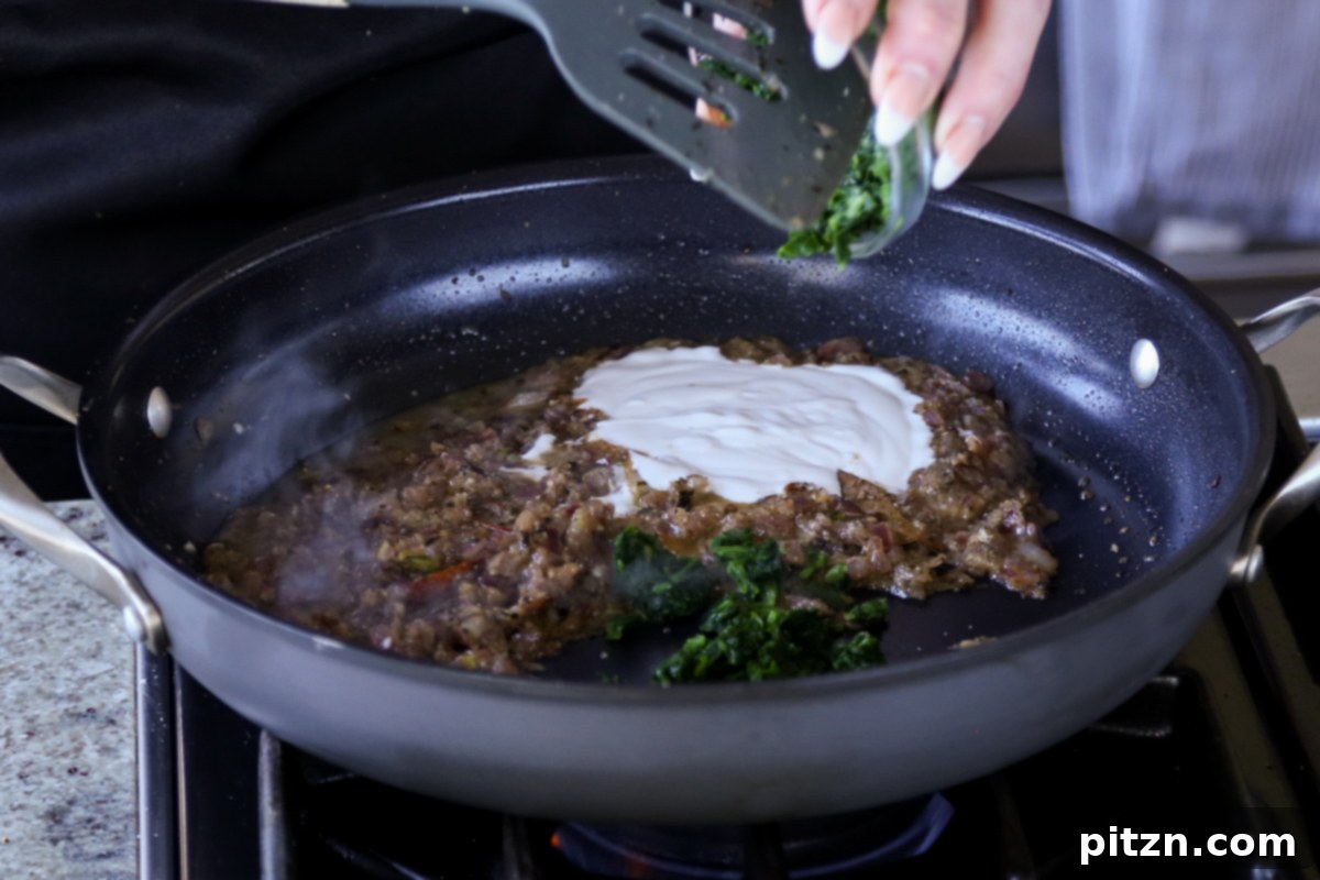 Adding non-dairy yogurt and spinach to the simmering spice and onion mixture in the pan, beginning to form the creamy sauce.